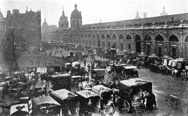 DELIVERING MEAT AT SMITHFIELD TODAY

There is an inclined road by the tree in the center of the picture, leading
to the special railroad freight depot. Cars are also run directly under the
market and their cargoes are delivered by hydraulic lifts to the stands above.